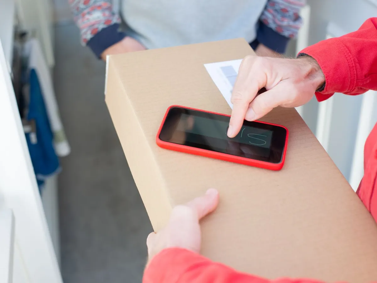 A driver holding a phone out at a doorway for a signature.