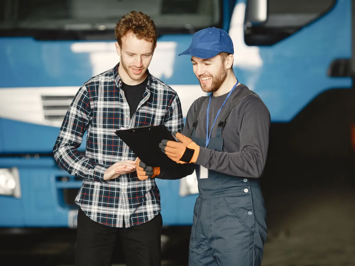 Two people reading a clipboard together beside a lorry, the person who runs the link checking the design before anything is built.